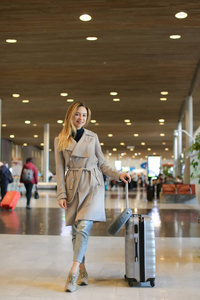 女人站在机场候诊室, 带手提箱, 身穿灰色大衣