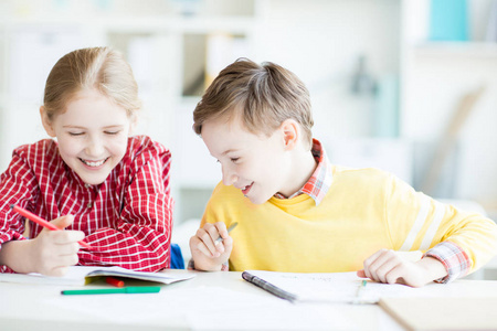 两个快乐的孩子看图片在女孩的抄写, 而坐在办公桌上的绘画课