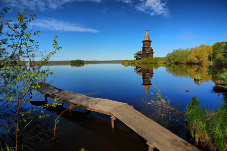 春天的风景与一个老木教会和一座桥梁在岸边镜子光滑的湖