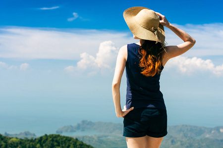 年轻的旅行妇女戴着帽子站在山顶上的悬崖上