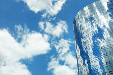 现代办公中心大楼的圆形镜面玻璃。晴朗的蓝天和窗外的倒影
