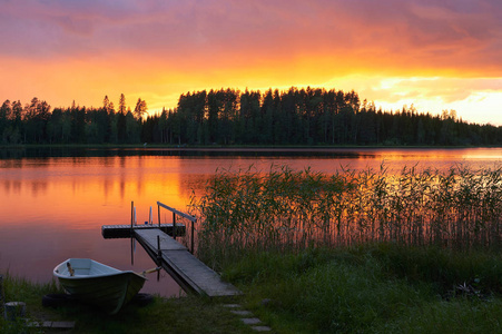 夏季日落的芬兰湖岸边, 一个小码头和一条小船