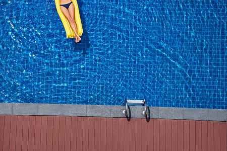 在大游泳池的黄色空气床垫上苗条的年轻妇女的顶部视图