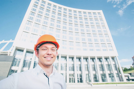 英俊的男人微笑着年轻中站在户外对建筑结构的安全帽