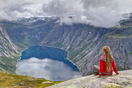 女孩坐在岩石和看挪威山风景。Trolltunga 岩石的踪迹。Ringedalsvatnet 湖, 挪威