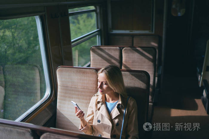 坐在靠窗的火车旁边的年轻漂亮女人使用智能手机