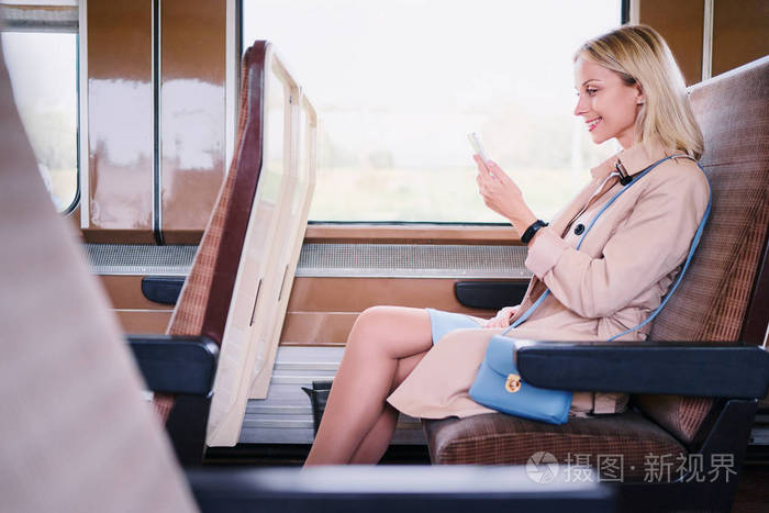 坐在靠窗的火车旁边的年轻漂亮女人使用智能手机