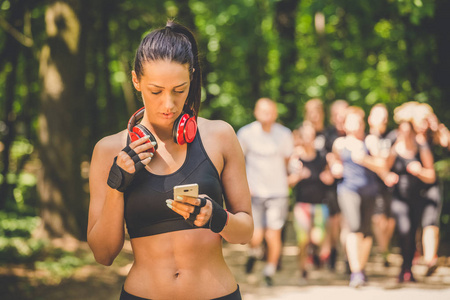 年轻女子在慢跑和使用智能手机的自然放松。背景中的赛跑者