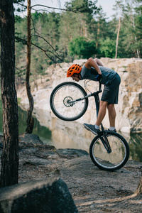 年轻的自行车车手平衡在后轮户外在湖前的森林