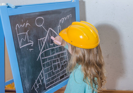 儿童工程师, 设计师, 戴头盔的女孩在黑色粉笔板上粉刷房子