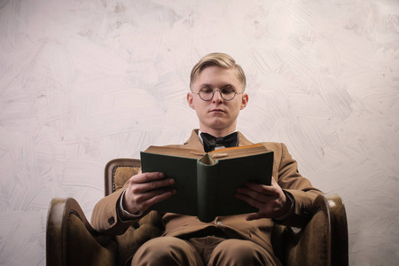优雅的年轻金发男子与眼镜和弓领带, 阅读一本旧书