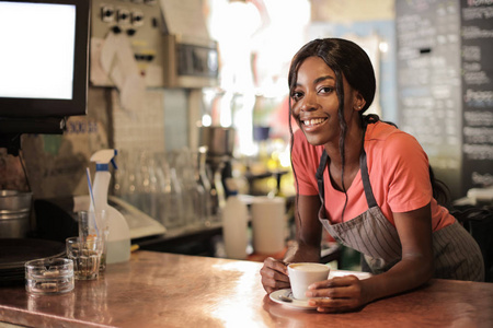 年轻美丽的非洲妇女作为服务员服务卡布奇诺和微笑