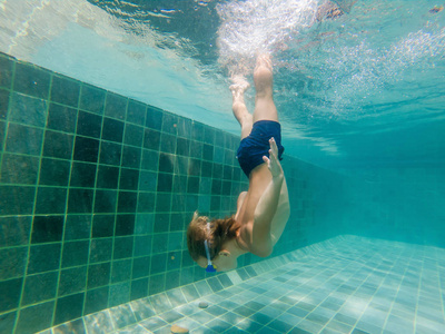男孩在水下游泳在水池里, 微笑和举行呼吸, 与游泳玻璃