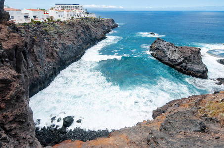 在大西洋上, 有大浪和黑色的悬崖, 边缘有房子。Gigantes 的度假村 巨人之崖。加那利群岛, 特内里费岛, 西班牙