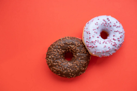 两个釉面甜甜圈被隔离在红色背景上. 柔和的颜色, 粉红色和棕色甜甜圈, 选择性聚焦。复制空间。简约理念