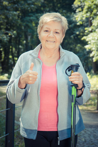 穿着运动服装的老年妇女手持北欧手杖, 竖起大拇指, 健康运动生活方式对老年人新鲜空气的概念