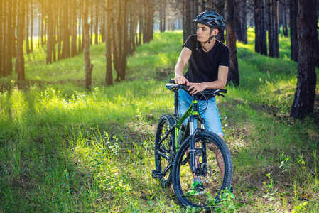 骑自行车的人坐在一辆绿色的山地自行车上, 在树林中的树丛中。积极健康的生活方式概念