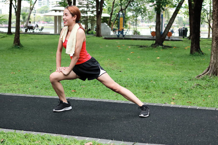 幸福亚洲妇女在公园奔跑之前伸展她的腿。健身与锻炼理念