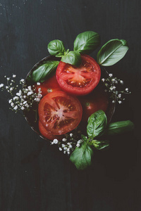 红色有机西红柿在碗里的花和罗勒叶子的顶部视图