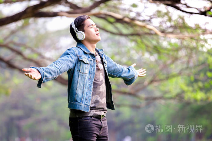 亚洲年轻人站在大自然的怀抱里, 用耳机听音乐