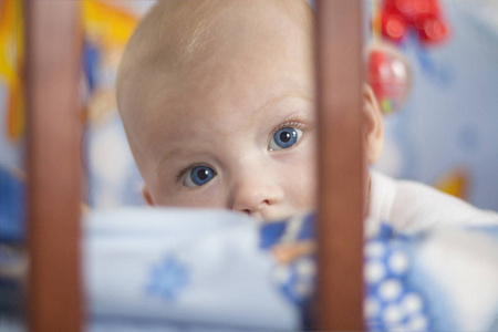 蓝眼睛金发女郎在婴儿床上偷看。窄焦点