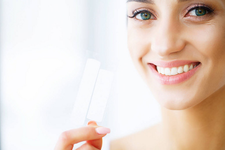女人用牙齿美白带为美丽的白色微笑。高分辨率图像