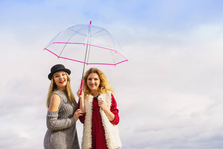 两个时髦的女人穿着时髦的衣服, 拿着透明的雨伞在户外消磨闲暇时间