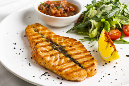 大鲑鱼牛排红鱼在烧烤与柠檬, 酱油与蔬菜和绿色的白色盘子