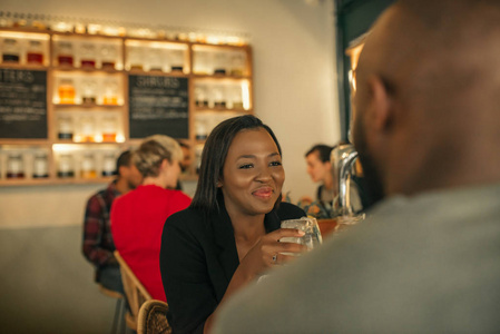微笑着年轻的非洲裔美国妇女坐在一个时髦的酒吧与她的男朋友享受饮料, 而在一起约会