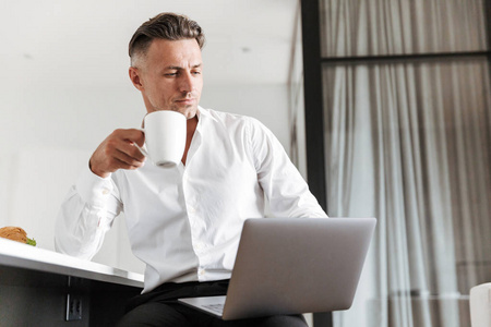 成功的人穿着正式的衣服使用笔记本电脑, 而坐在家里吃早饭