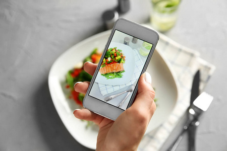 妇女用手机拍照新鲜沙拉和鱼