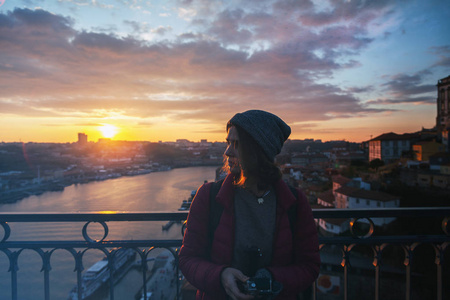 美丽的年轻女孩的游客站在日落俯瞰城市波尔图, 葡萄牙, 在夕阳的光芒