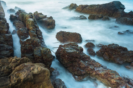 长的暴露海景与泡沫波浪飞溅对泰国的岩石海岸在早晨时间