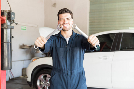 微笑的男性修理工显示组合扳手对汽车在车库