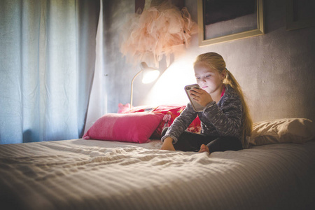美丽的金发女孩躺在床上, 看着智能手机上的视频