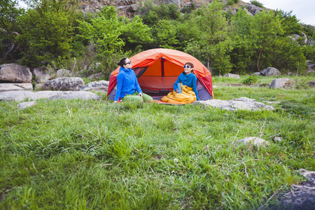 两个女孩坐在帐篷里。女朋友在大自然中交流。睡袋里的女人喝咖啡。露营地的朋友们。微笑的黑发女郎谈话