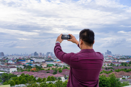 年轻男子在胭脂红衬衫拍照的城市景观与他的手机