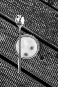 从上面的一杯拿铁 machiato 站在阳台上, 上面放着一只银色的勺子, 它在玻璃上。白色泡沫可以看到, 老露台板与凹槽