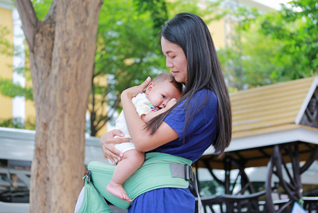 亚洲母亲抱着婴儿在人体工程学婴儿载体