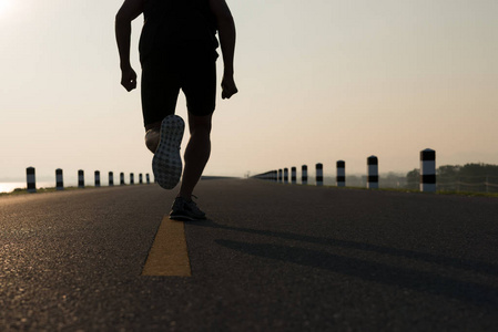 人亚洲腿的下来看法在时间奔跑在日出期间在水坝路锻炼。健康的生活方式