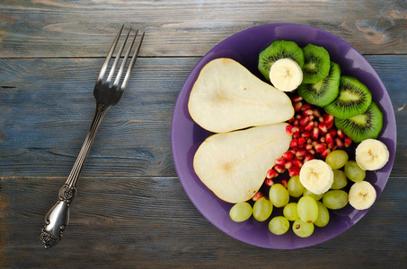 在木制背景下的水果混合 梨, 猕猴桃, 葡萄, 香蕉, 石榴。盘子里的水果