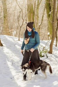 时尚的女人穿着滑稽的帽子走在公园与她的西伯利亚沙哑的狗拴在皮带上