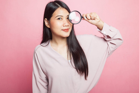 年轻的亚洲妇女与放大镜在粉红色背景