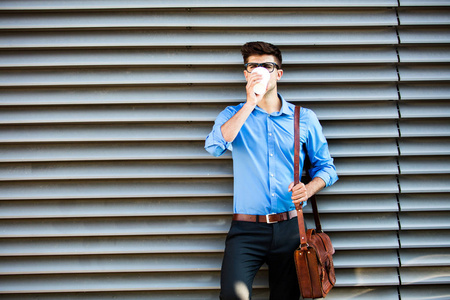 办公室的人用眼镜去工作与皮革袋在办公室前喝一杯咖啡, 在外面的某个地方