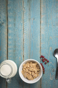有机玉米或燕麦或谷类或大麦片在蓝色瓷碗与红色醋栗和牛奶罐在老木桌上
