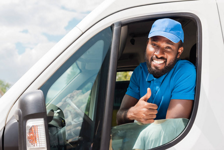 微笑的非洲美国人送货人显示拇指从汽车