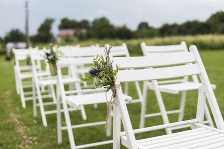 白色的婚礼椅, 在绿色的草地上点缀着鲜花。为婚礼准备的花园绿色草坪上的客人空木椅