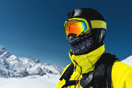 特写肖像滑雪者在面具和头盔与一个封闭的脸, 在积雪的山脉和蓝天背景下