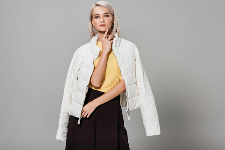 灰色背景下的肩上白色夹克上的自信年轻女性模特