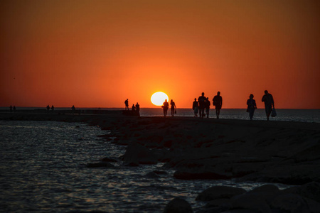 人们在海边的 brakewater 享受夕阳。温暖的夏日傍晚, 匿名人士步行和放松。轮廓